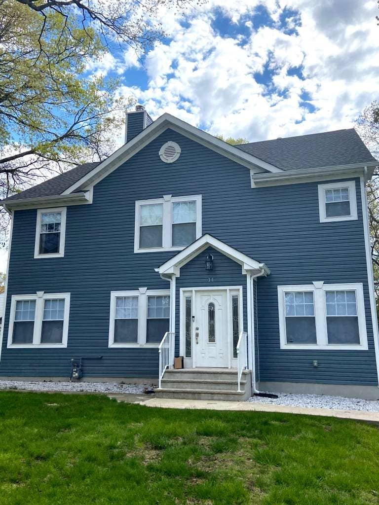 Newly renovated two-story residential home with gray siding, stone front steps, and modern entryway installed by Legacy Contractor NJ.