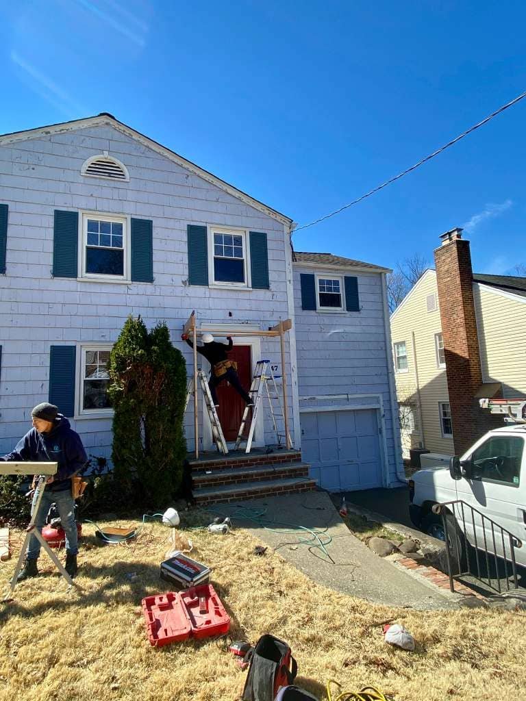 Workers installing exterior siding on a two-story residential home using scaffolding and ladders during a home renovation project.