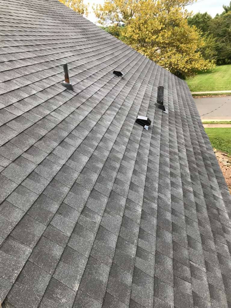 Gray asphalt shingle roof with multiple vent pipes and attic ventilation installed on a sloped residential rooftop.