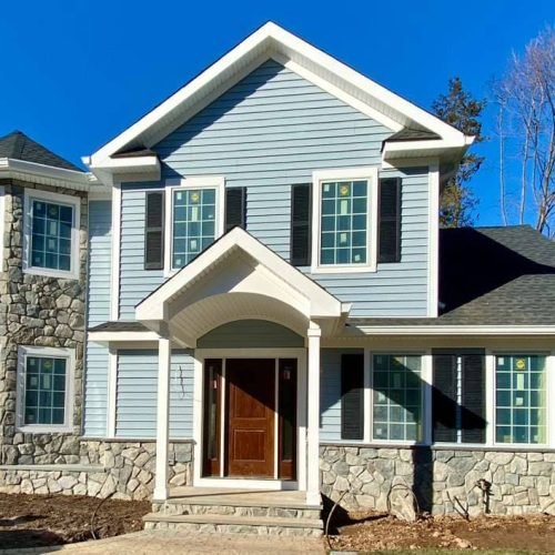 Front view of newly constructed two-story home with blue siding, stone veneer accents, and arched entryway installed by Legacy Contractor